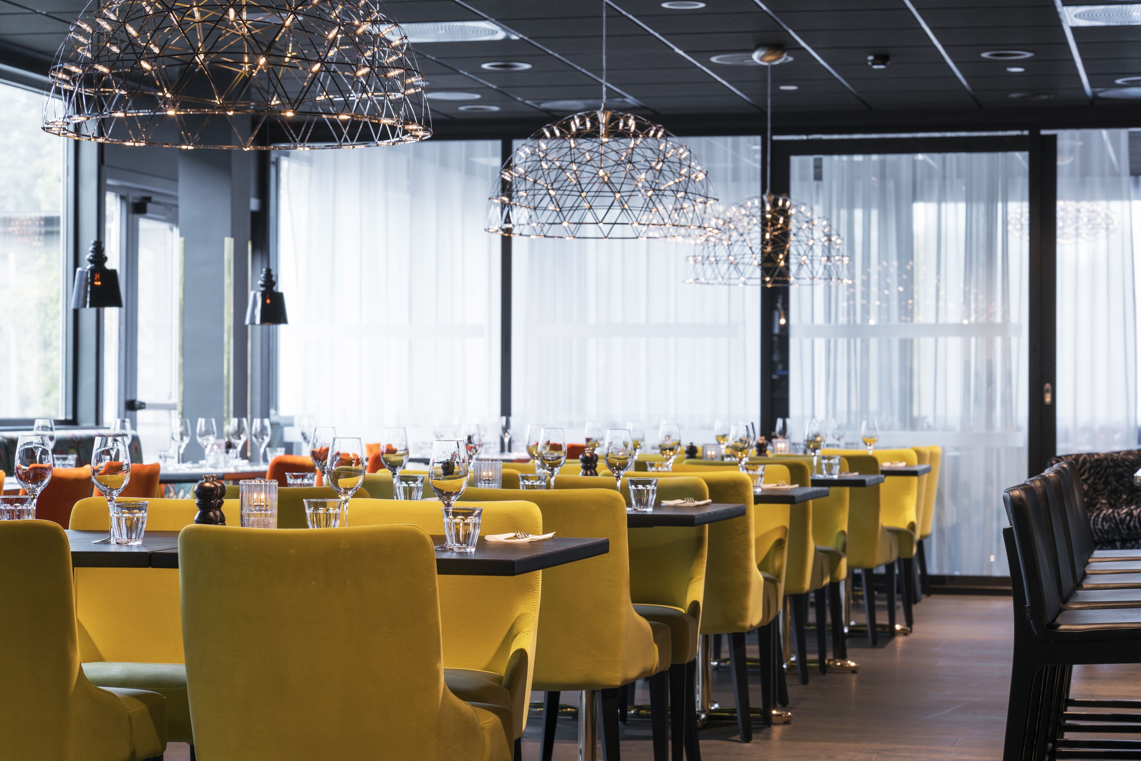 A restaurant with yellow chairs and tables, modern pendant lights, and large windows.