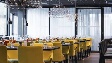 A restaurant with yellow chairs and tables, modern pendant lights, and large windows.
