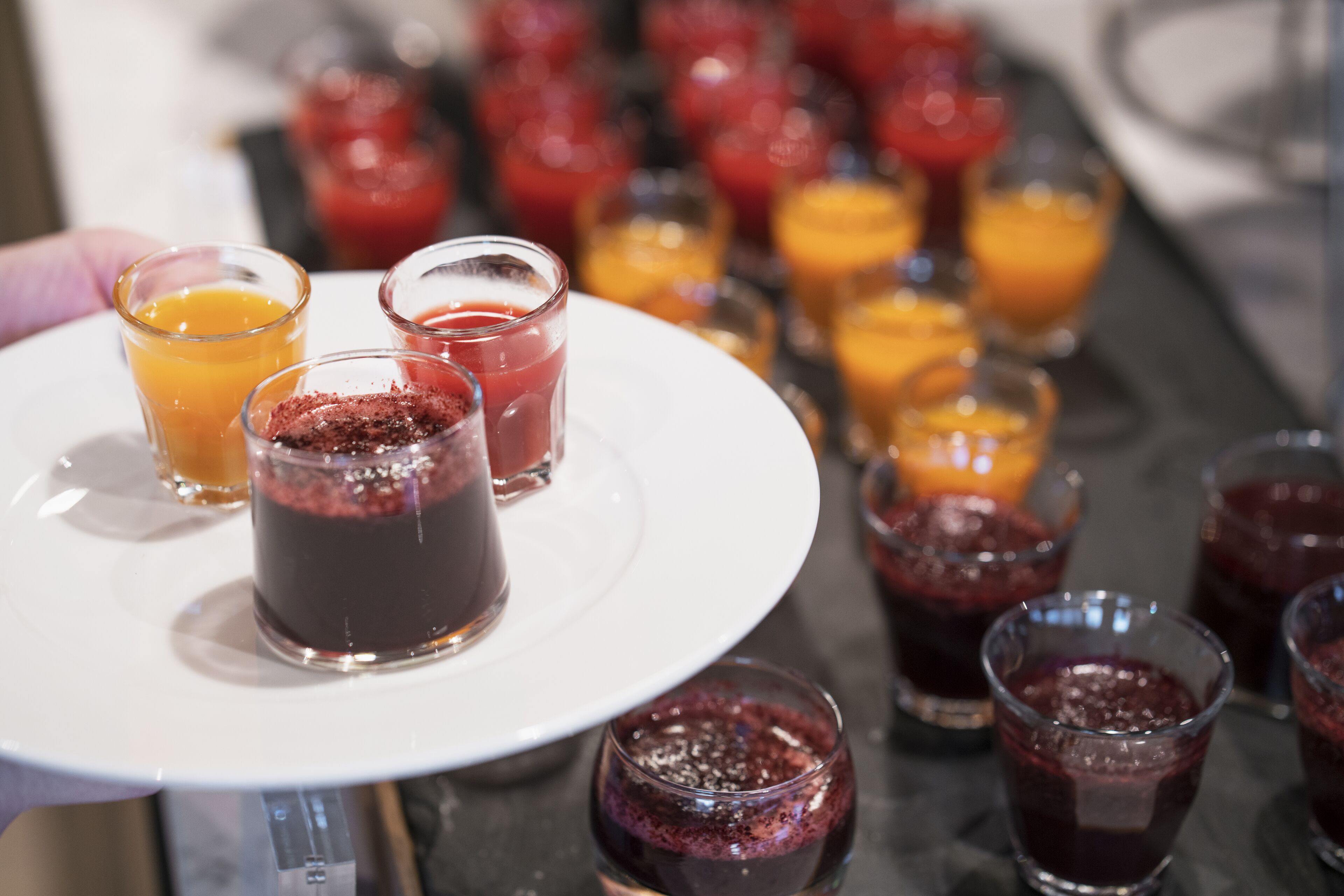 A tray of various beverages, including juices and possibly cocktails, arranged on a white plate.