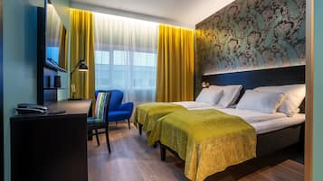 A hotel room with a bed, two bedside tables, a desk with a lamp, a chair, and a large window with curtains.
