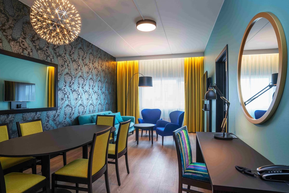 A hotel room with a dining area, a sofa, a TV, and a large mirror.