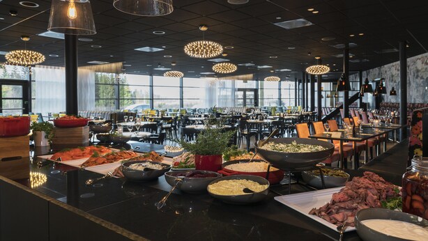 Un buffet proposant une variété de plats, ainsi qu’un intérieur moderne agrémenté de luminaires suspendus et de grandes fenêtres.