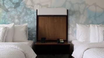 Quarto de hotel com duas camas, uma cabeceira de madeira, mesa de cabeceira com telefone e parede estampada com motivos florais.