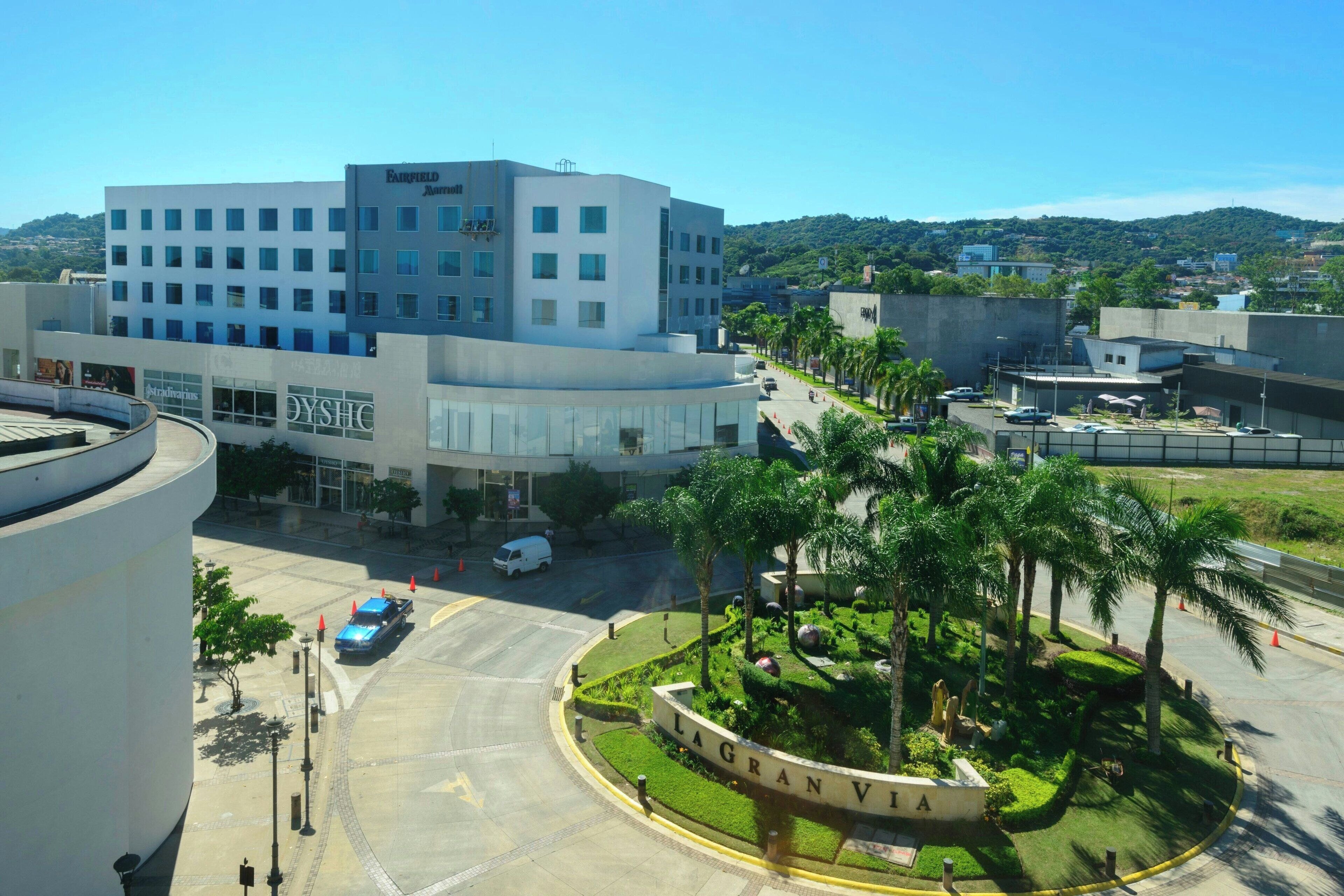 A modern hotel with a central courtyard, a parking area, and a view of the surrounding cityscape.