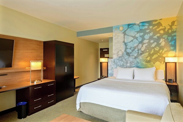 A hotel room with a large bed, a desk with drawers, a wardrobe, and a wall-mounted TV.