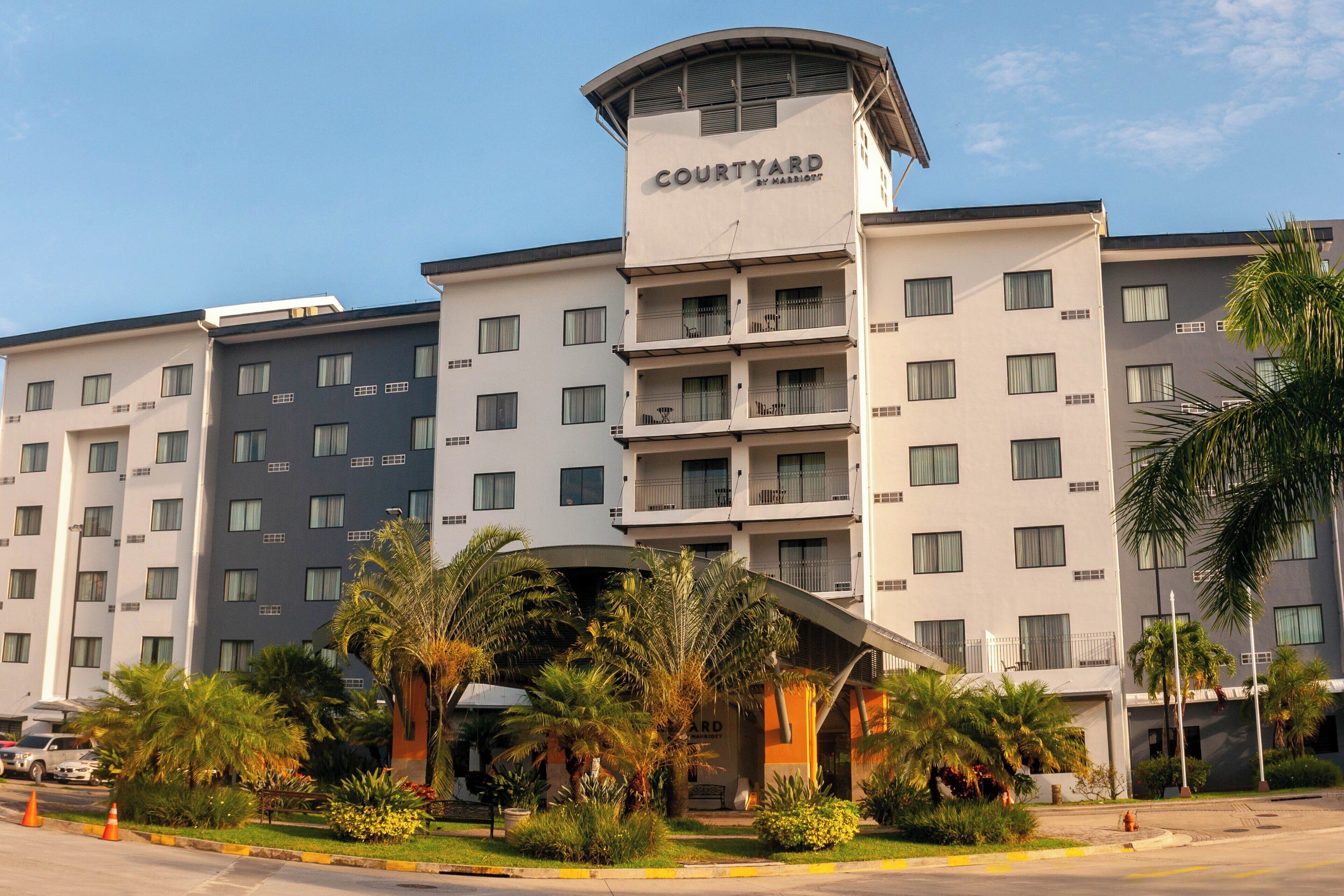 A multi-story hotel with a prominent 'Courtyard by Marriott' sign, featuring balconies and a central courtyard with palm trees.