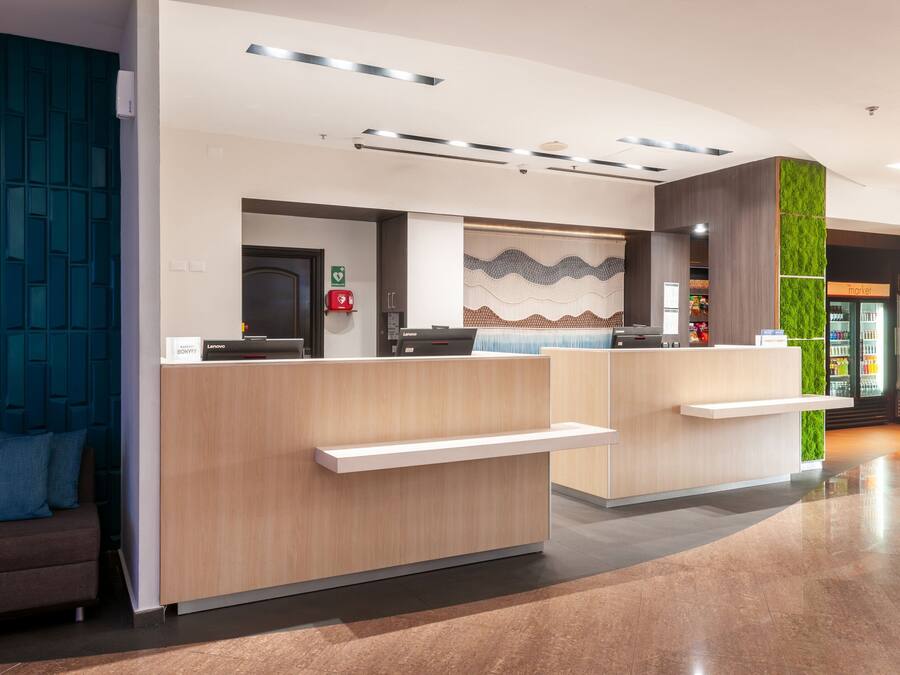 A modern reception desk with a light wood finish, a green vertical garden, and a patterned wall behind it.