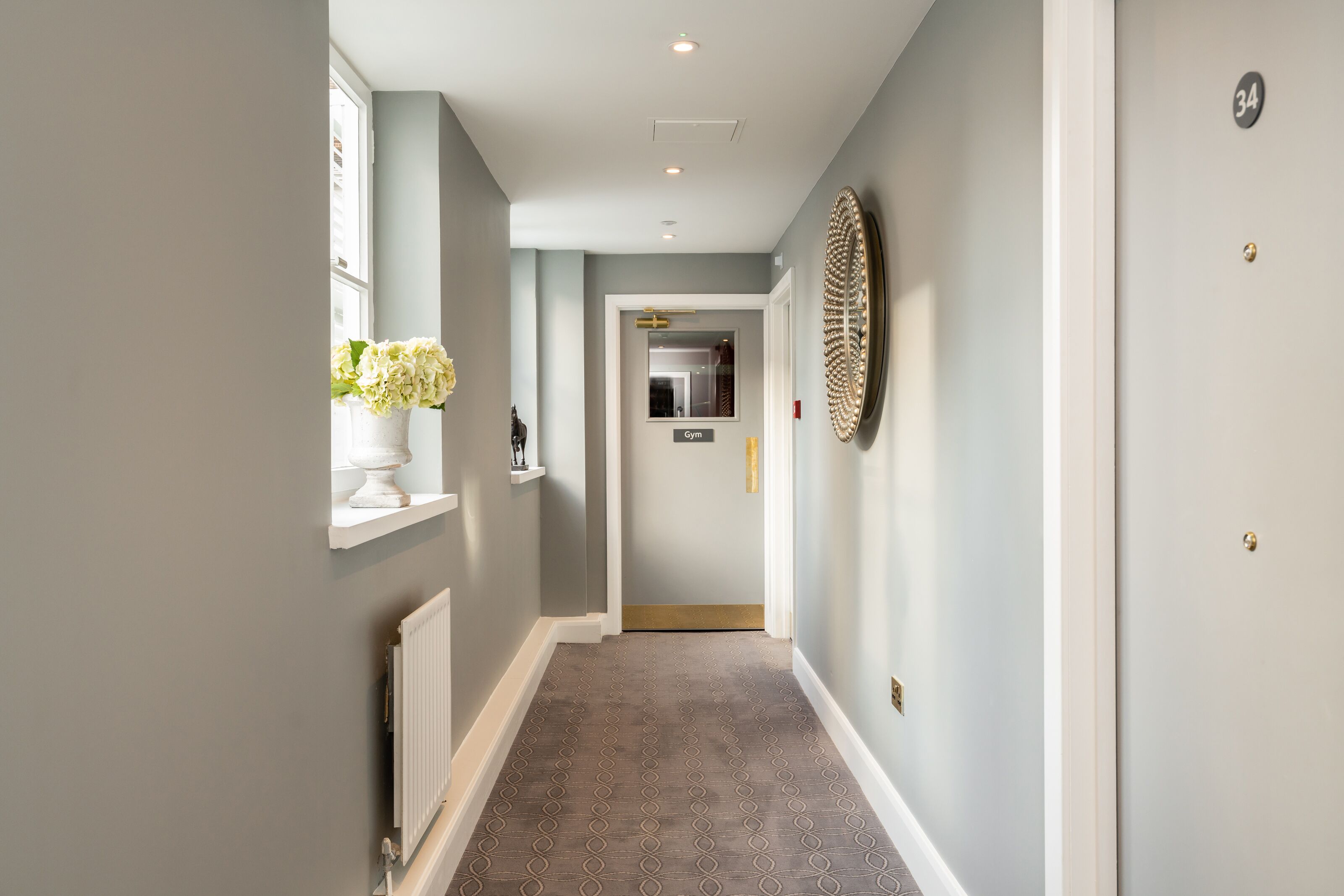 A hallway with a patterned carpet, a radiator, a wall-mounted mirror, and a door labeled "Gym".