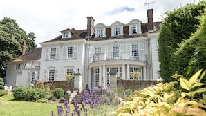A large, white, two-story house with a curved front, surrounded by well-maintained gardens and a lawn. - Gorse Hill (Woking)