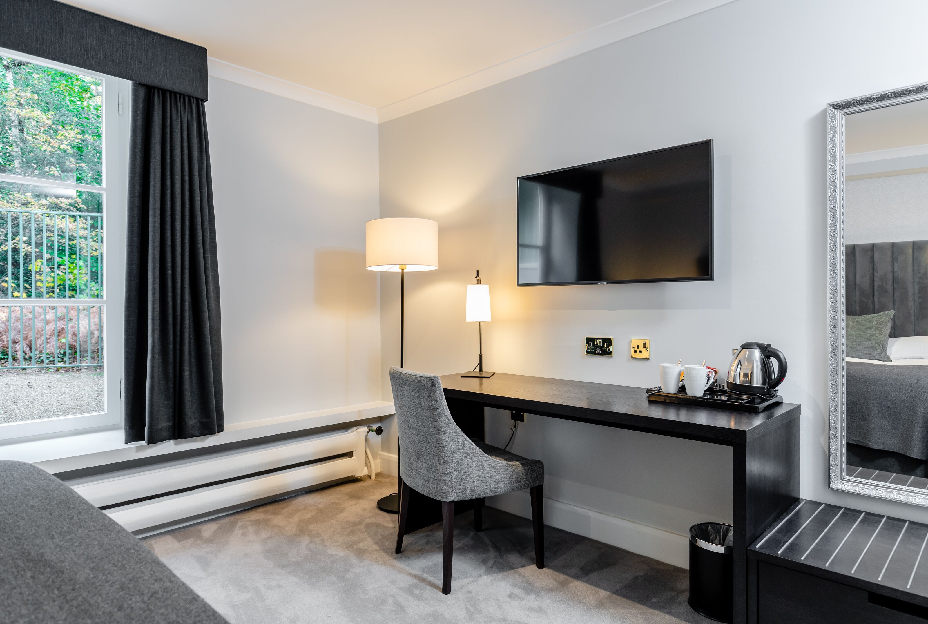 A modern hotel room with a desk, chair, TV, and a large mirror.