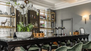 A bar area with a marble countertop, green velvet chairs, and a wine and liquor display. - Gorse Hill (Woking)