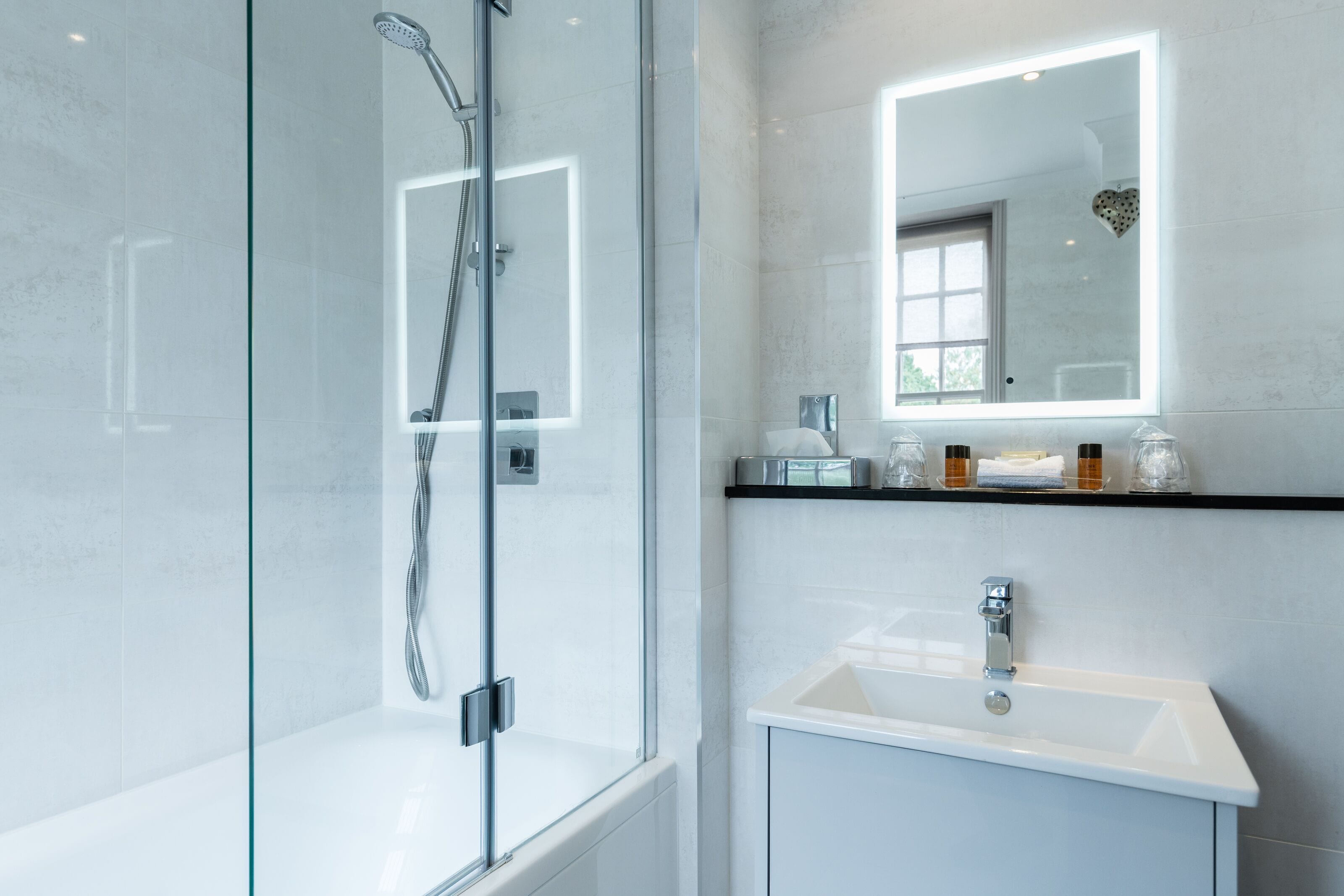 A modern bathroom with a glass-enclosed shower, a white sink, and a vanity with a mirror.