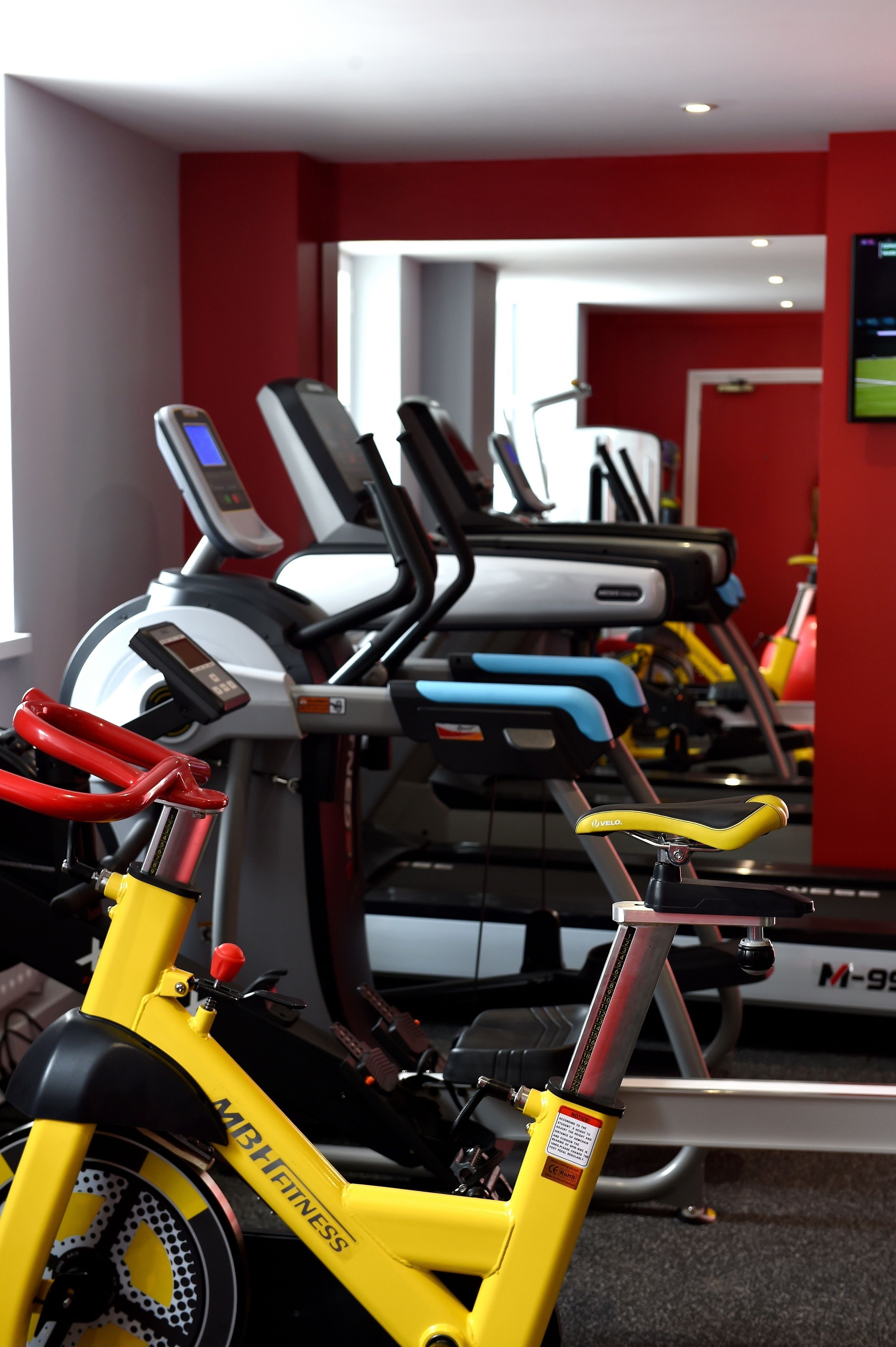 A gym with stationary bikes and treadmills, red walls, and a window.