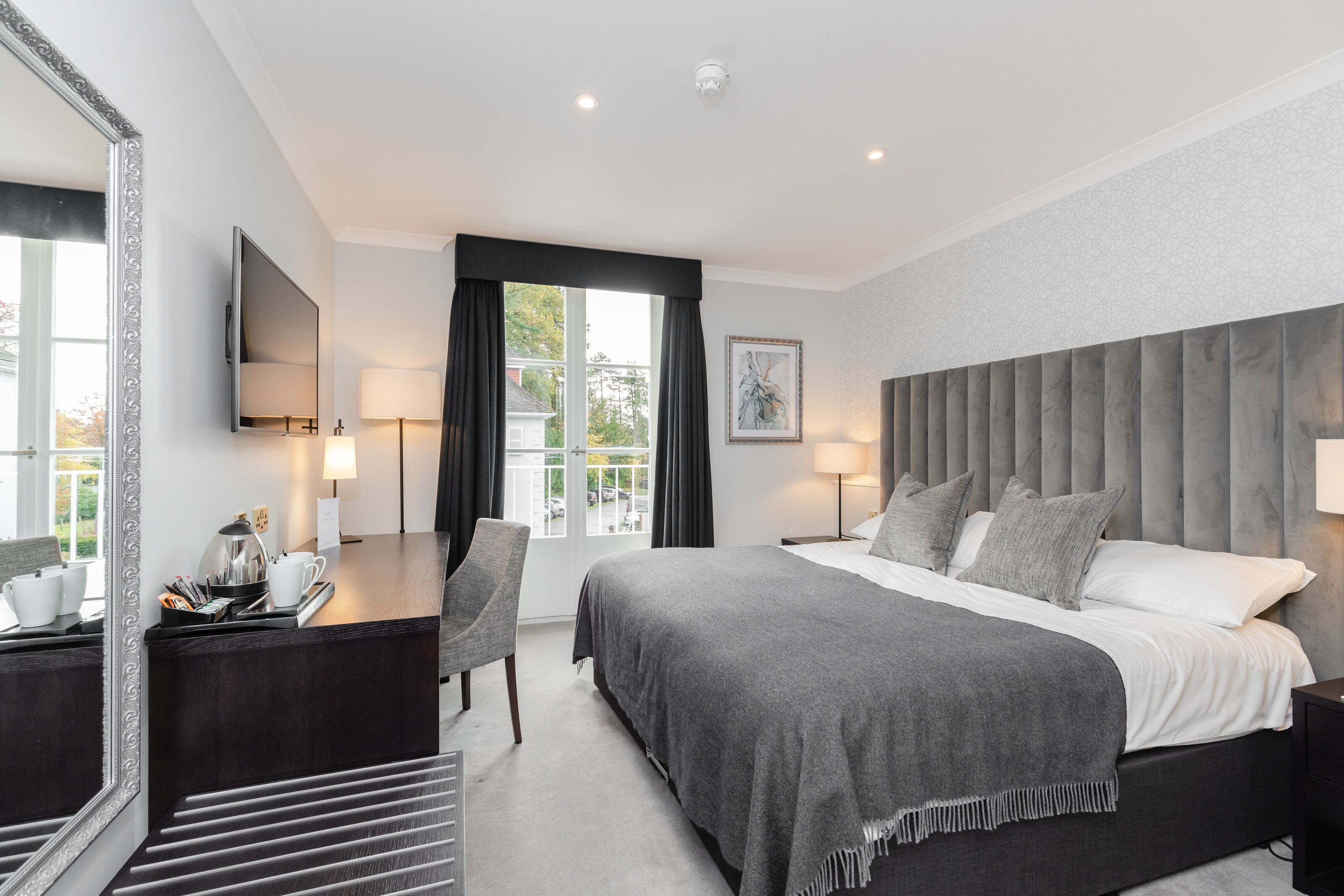 A modern hotel room with a large bed, a desk, a chair, a TV, and a window with curtains.