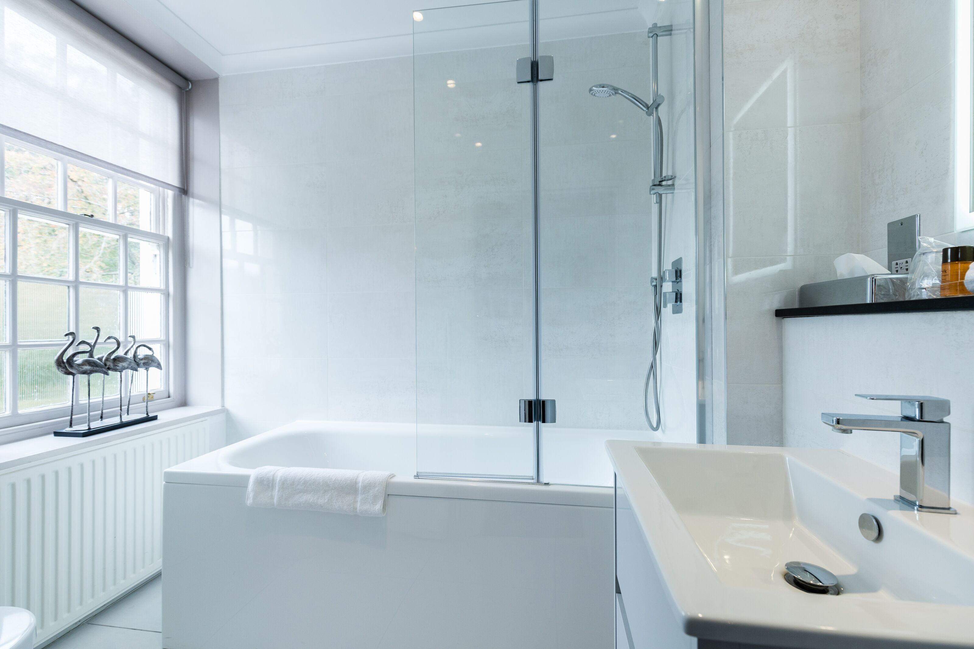 Un baño moderno con ducha de vidrio, una bañera blanca y un lavamanos con espejo.