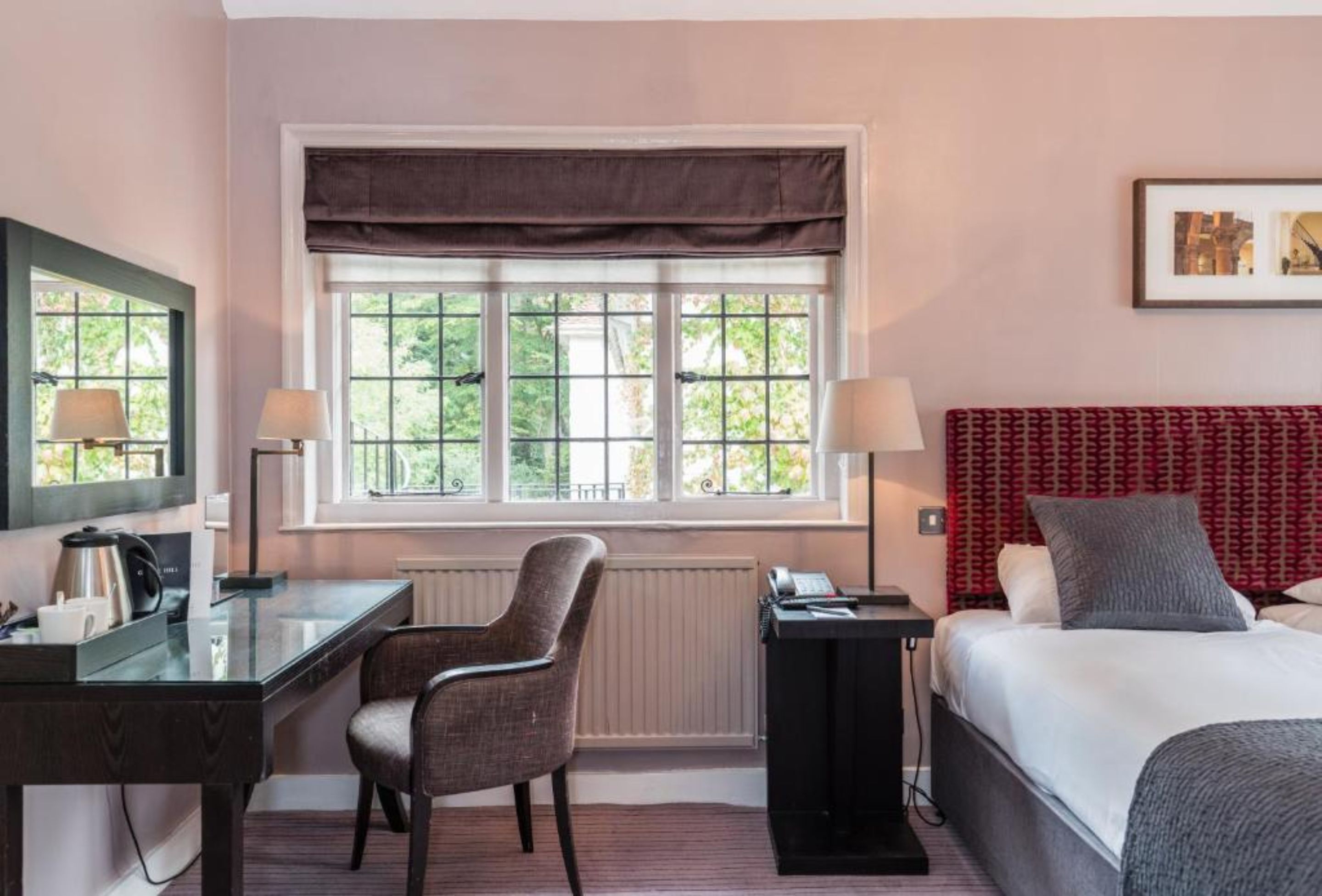 Habitación de hotel con cama, escritorio, silla, ventana con vistas a zonas verdes y un radiador.