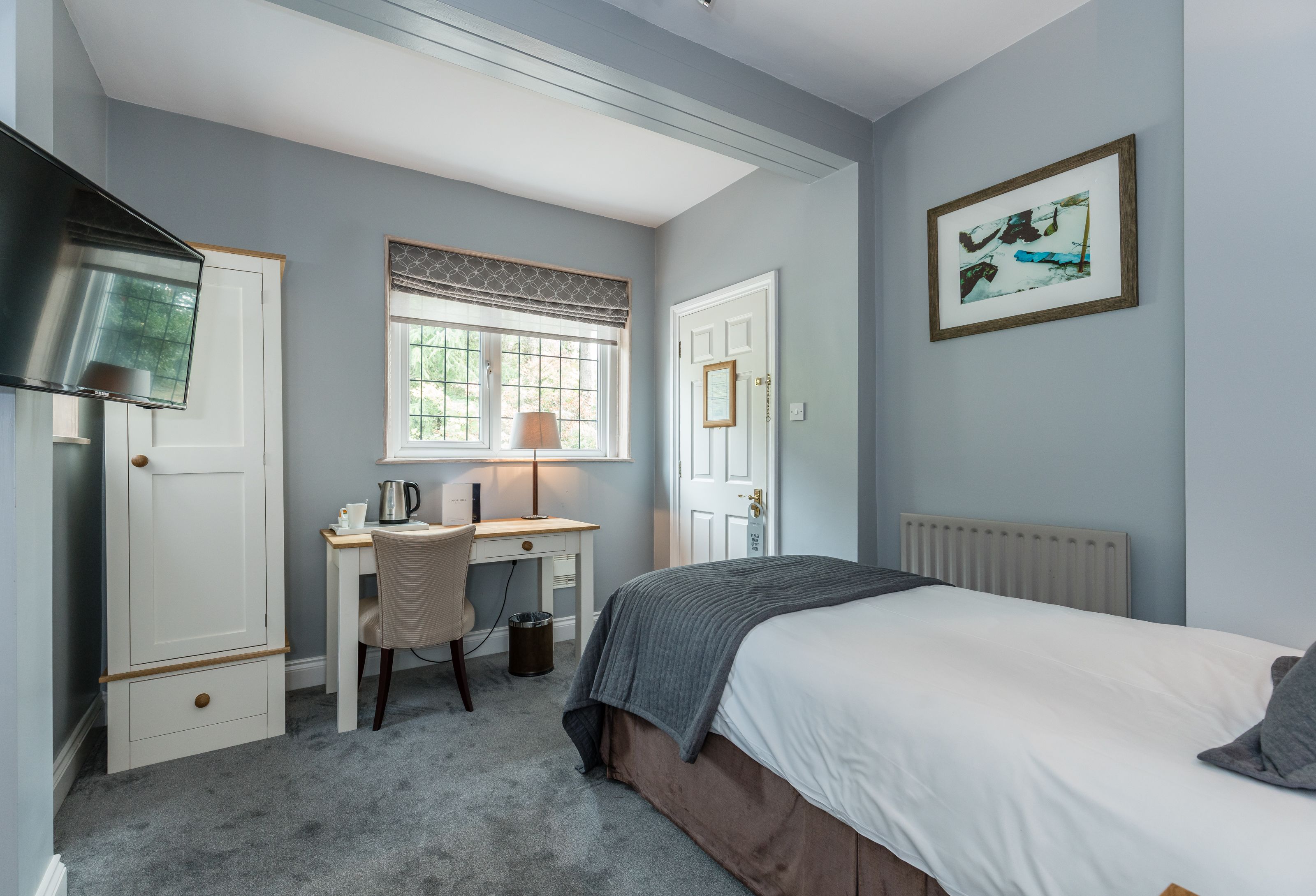A bedroom with a bed, a desk, a chair, a radiator, and a window with blinds.