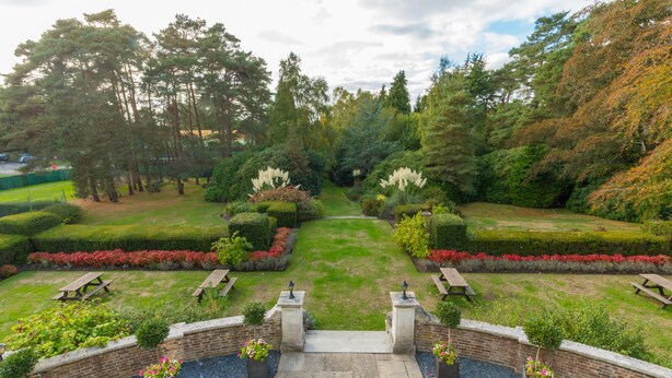 A well-maintained garden with a central pathway, benches, and a brick wall. - Gorse Hill (Woking)