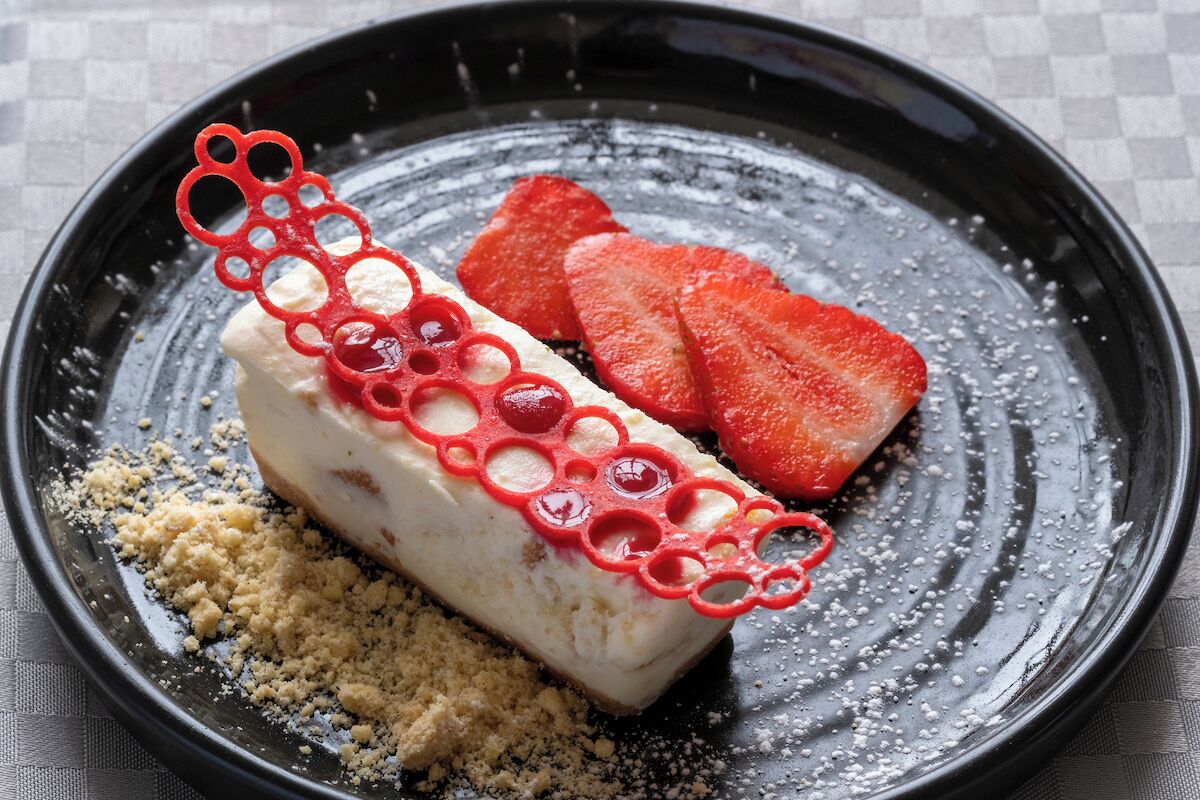 A dessert with a white base, red decorative elements, and strawberry slices on a black plate.