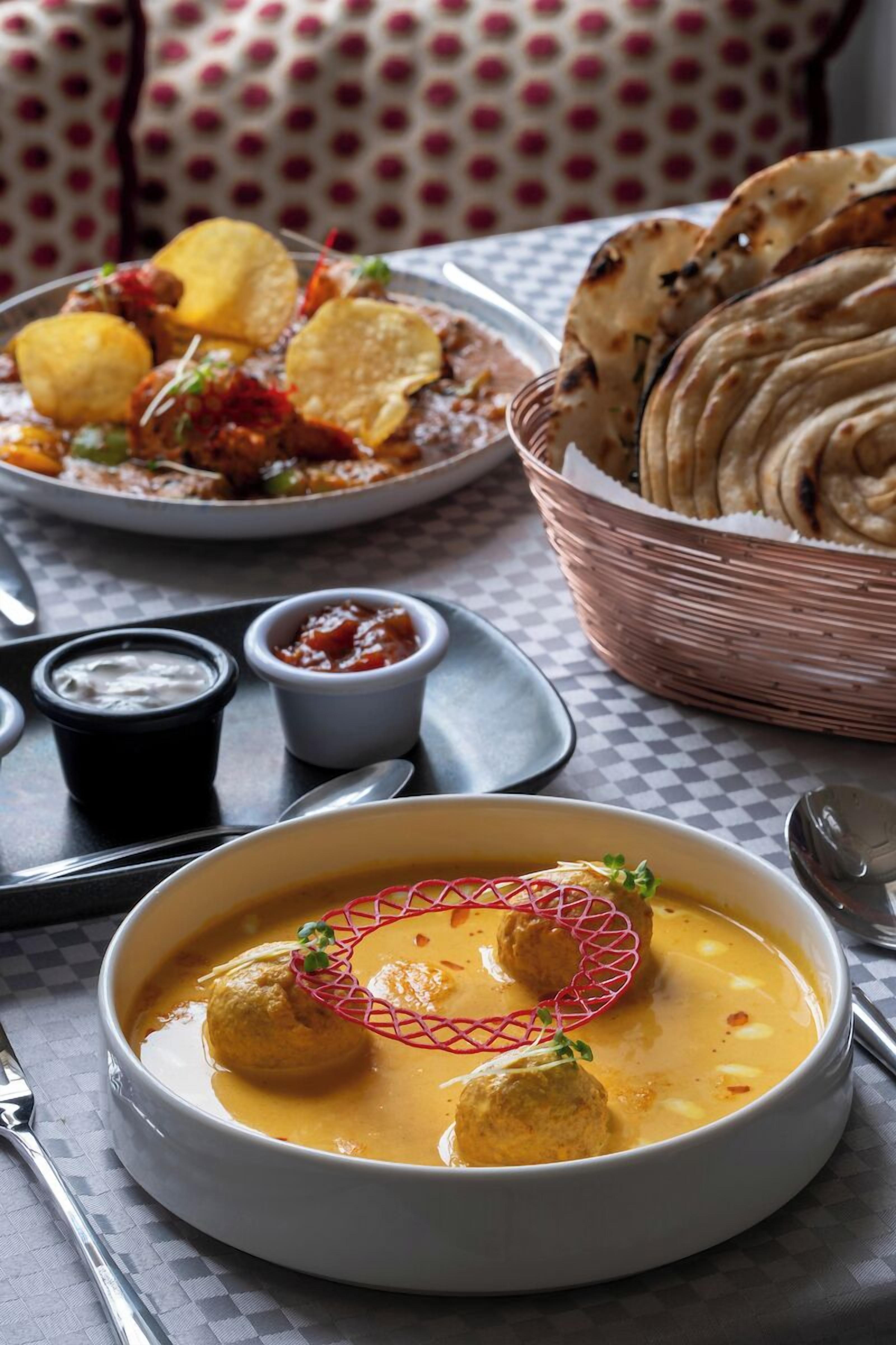 A bowl of curry with meatballs, a basket of flatbread, and a plate of chips with dipping sauces.