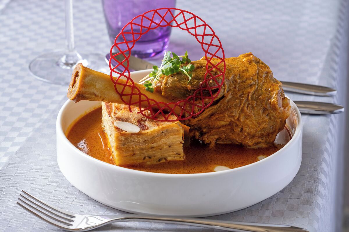 A bowl of curry with a bone and garnish on a white plate.