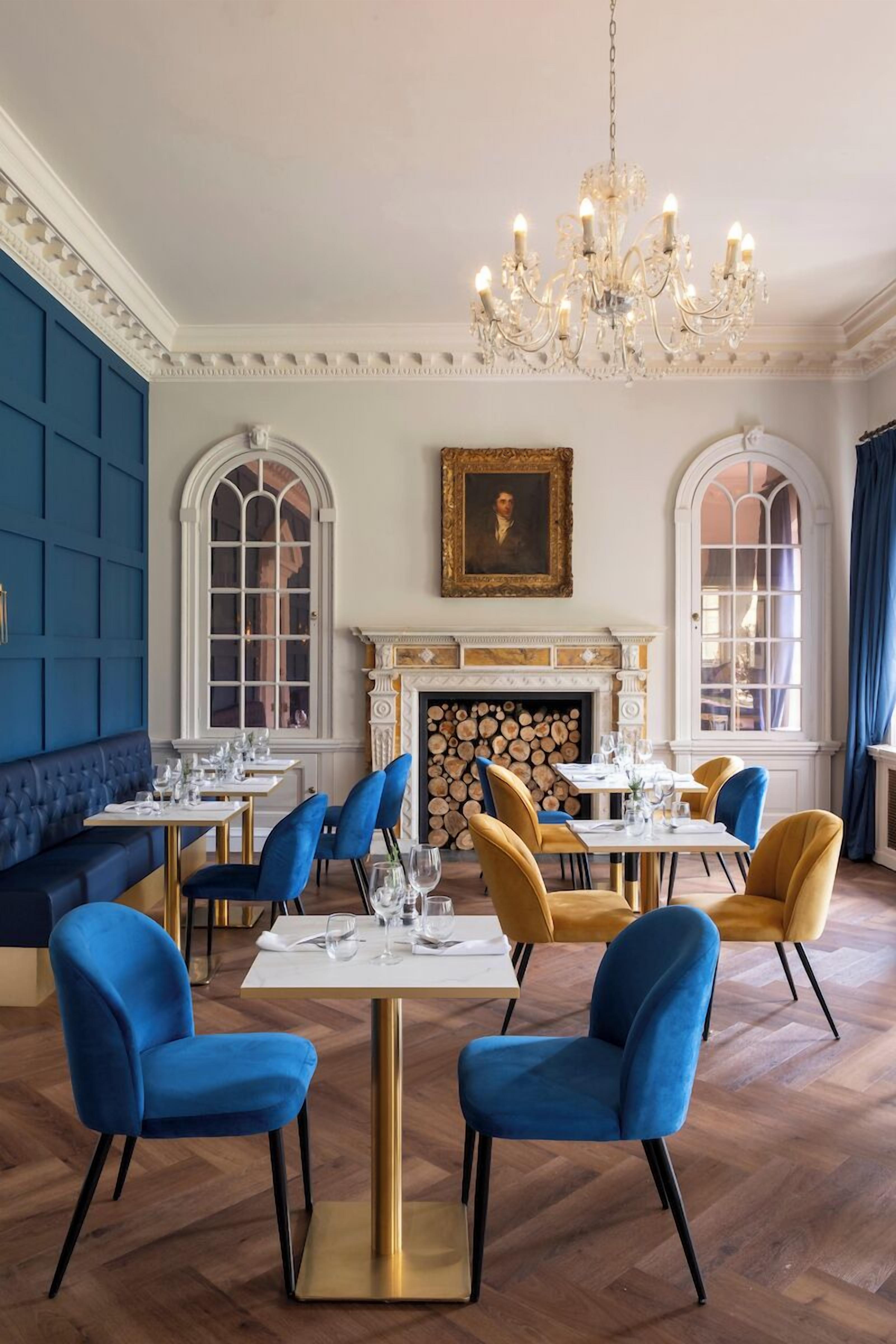 A dining area with blue and gold chairs, white tables, and a chandelier.