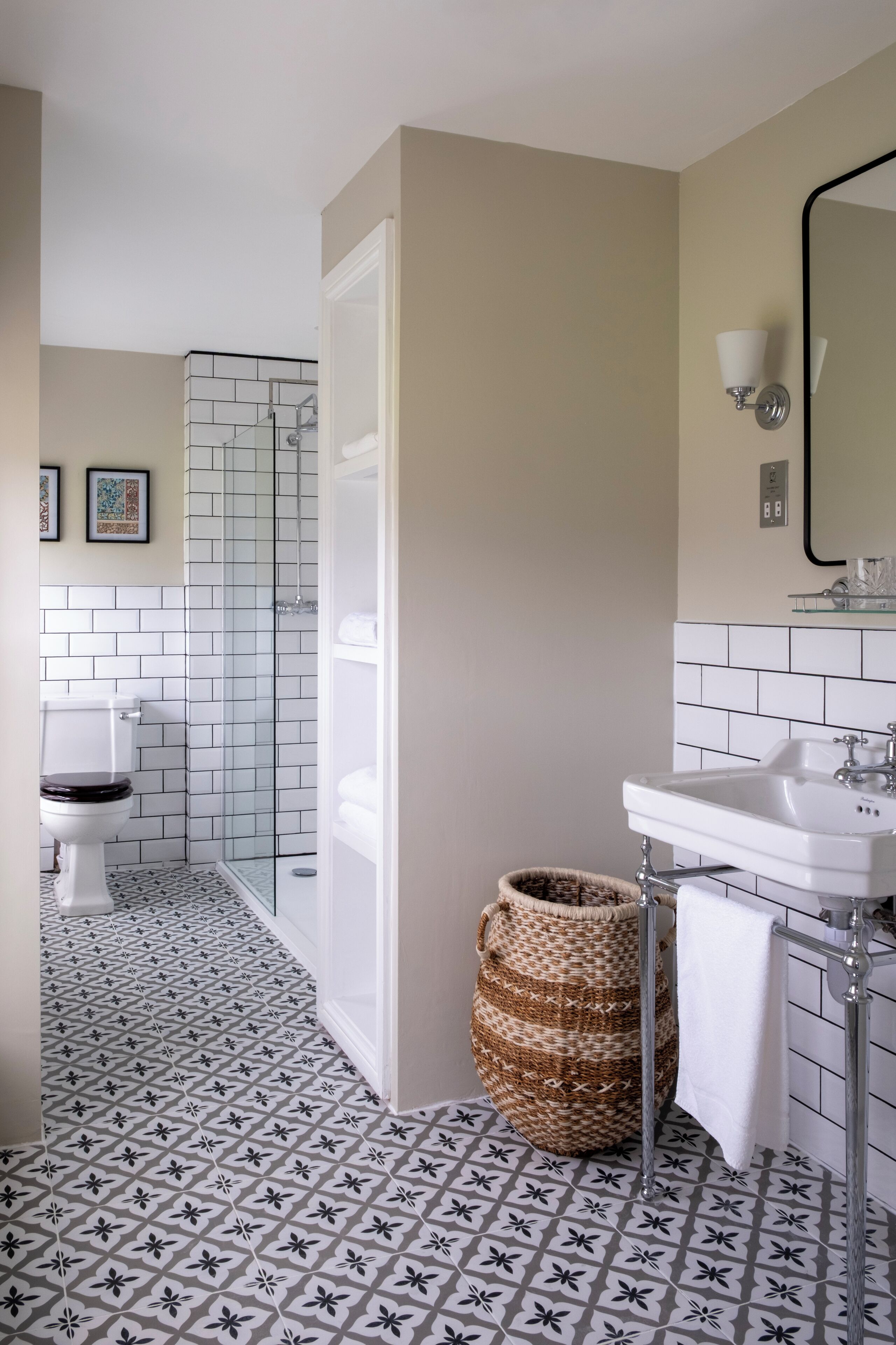 A bathroom with a white toilet, a glass shower enclosure, a sink with a mirror, and a patterned floor.