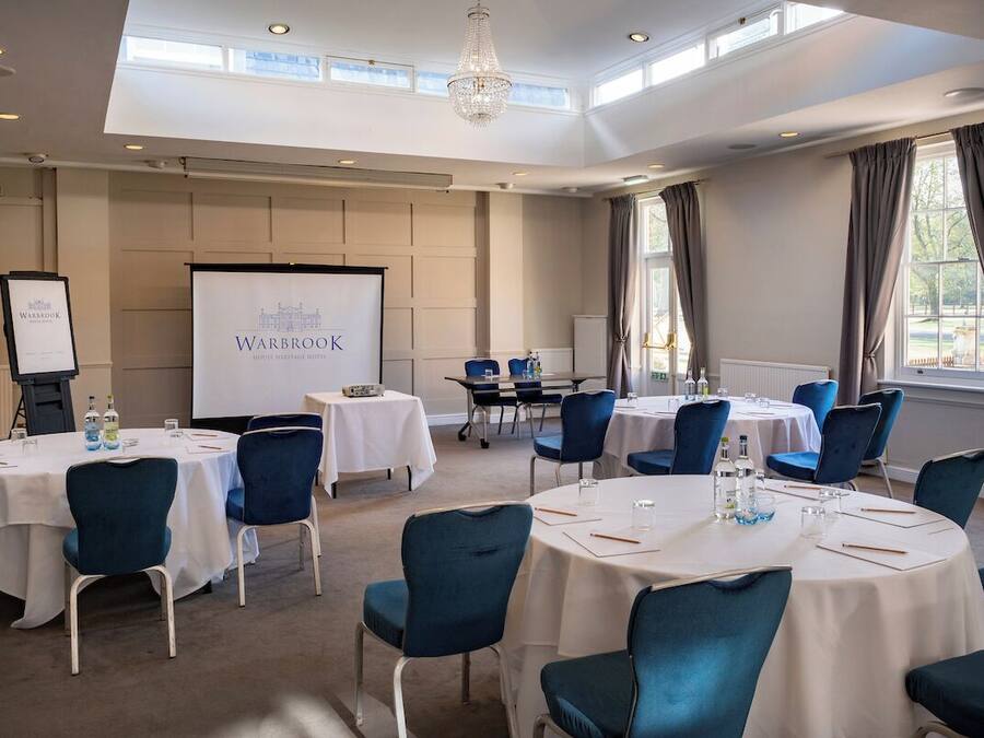 A conference room with round tables, blue chairs, a projector screen, and a chandelier.
