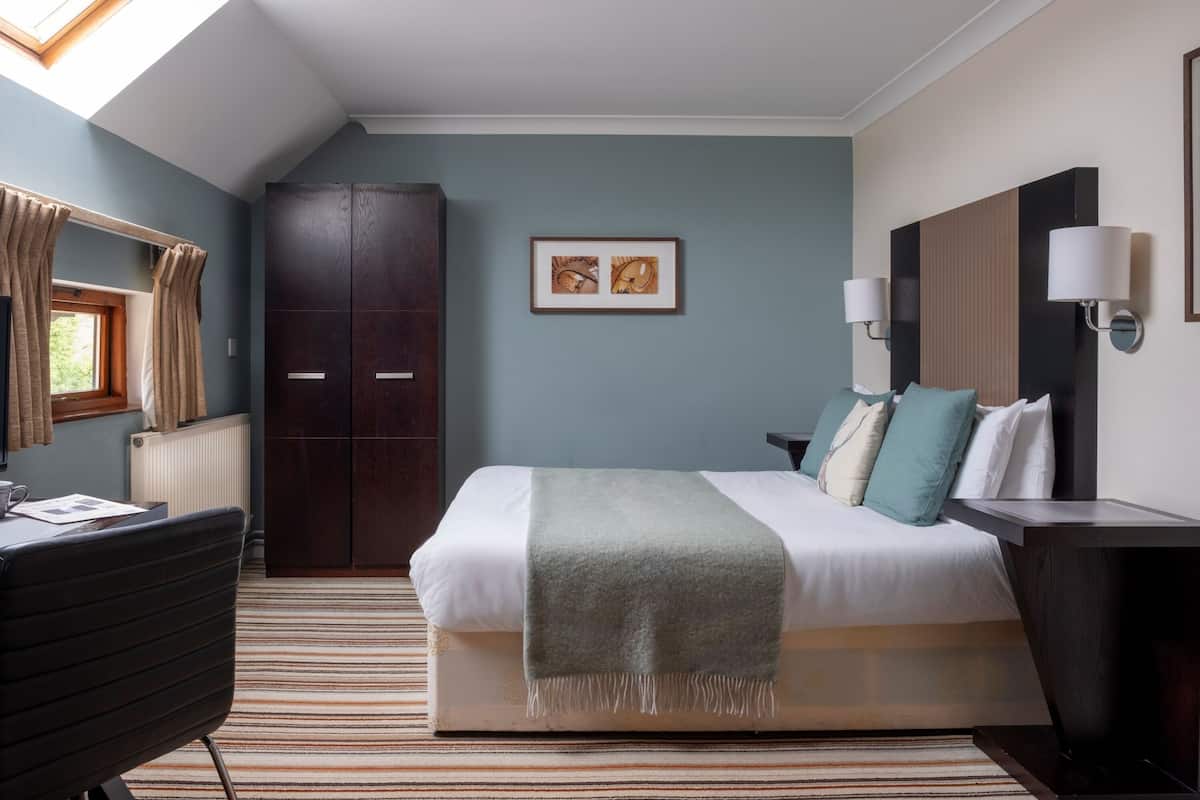 Habitació d'hotel amb un llit, escriptori, cadira, armari i un quadre al mur.