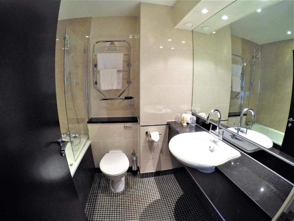 A modern bathroom with a glass shower enclosure, a white toilet, a sink with a mirror, and a tiled floor.