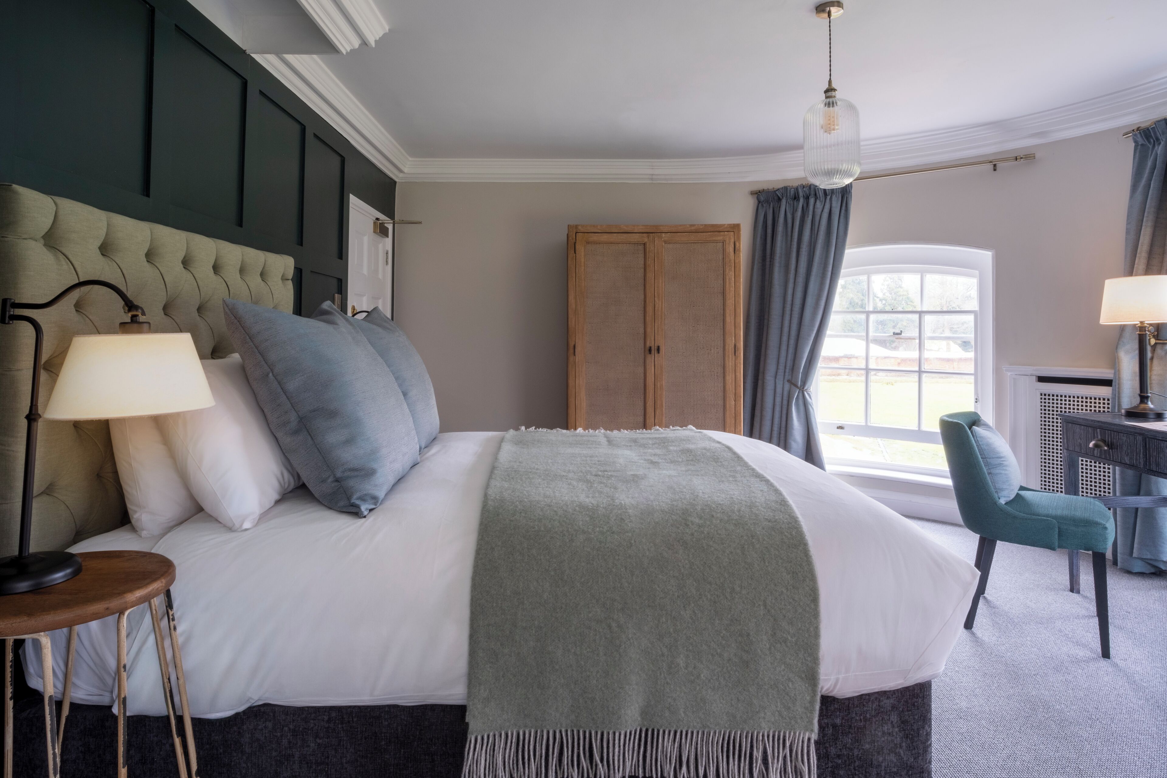 A neatly arranged bedroom with a large bed, a chair, a desk, and a window with curtains.