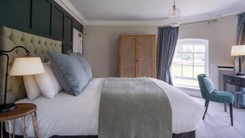 Un dormitorio ordenado con una cama grande, una silla, un escritorio y una ventana con cortinas.