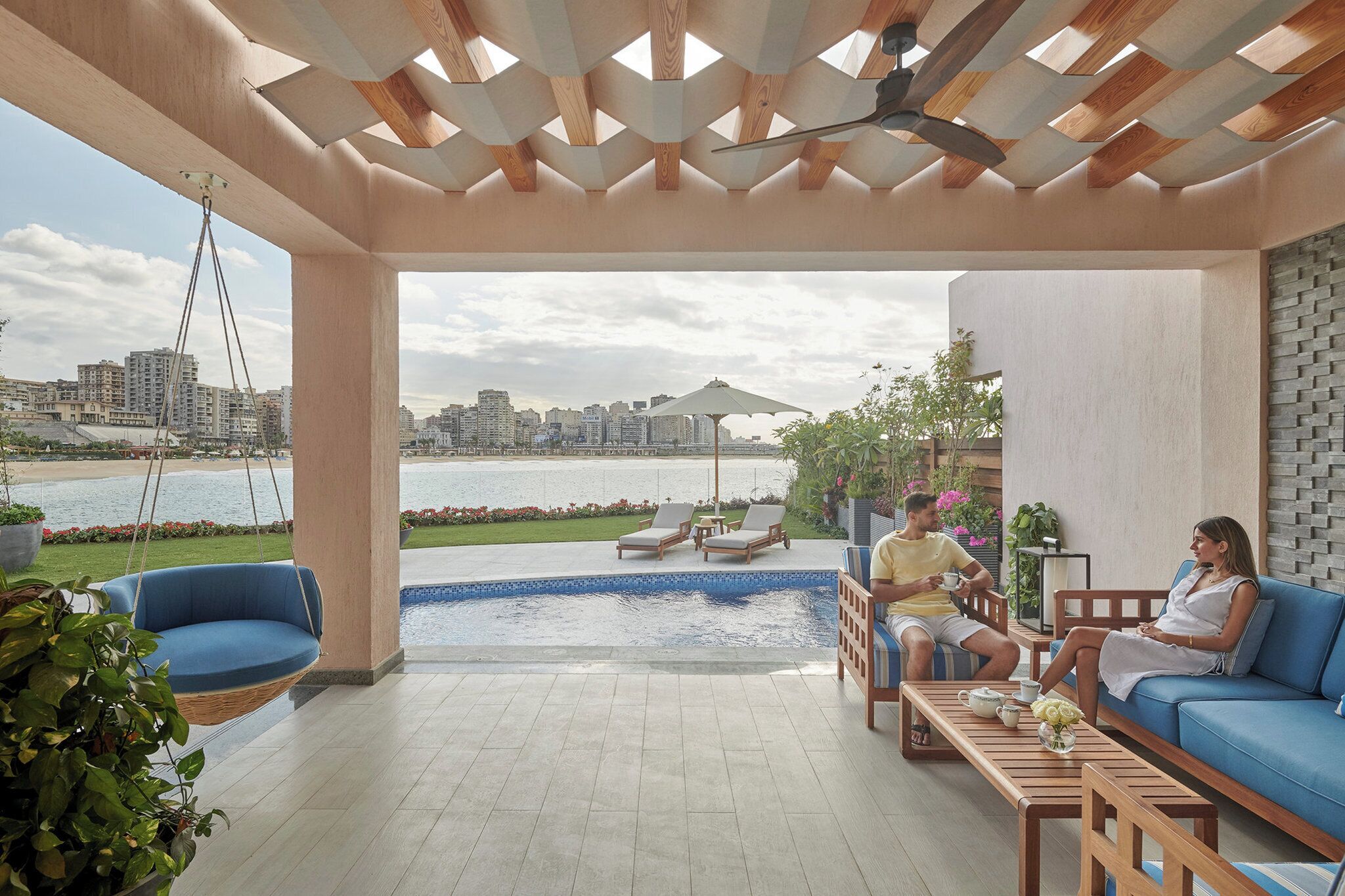 Uma área de estar moderna ao ar livre, com piscina, cadeira de balanço suspensa e vista para o horizonte da cidade.
