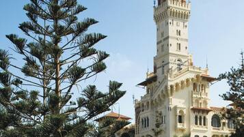 A tall, ornate tower with intricate architectural details, surrounded by lush greenery and a clear sky.