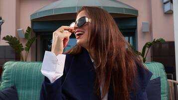 Une femme est assise à une table devant une assiette de nourriture, une tasse de café, et, en arrière-plan, on peut voir une enseigne sur laquelle est écrit « Fresca ».