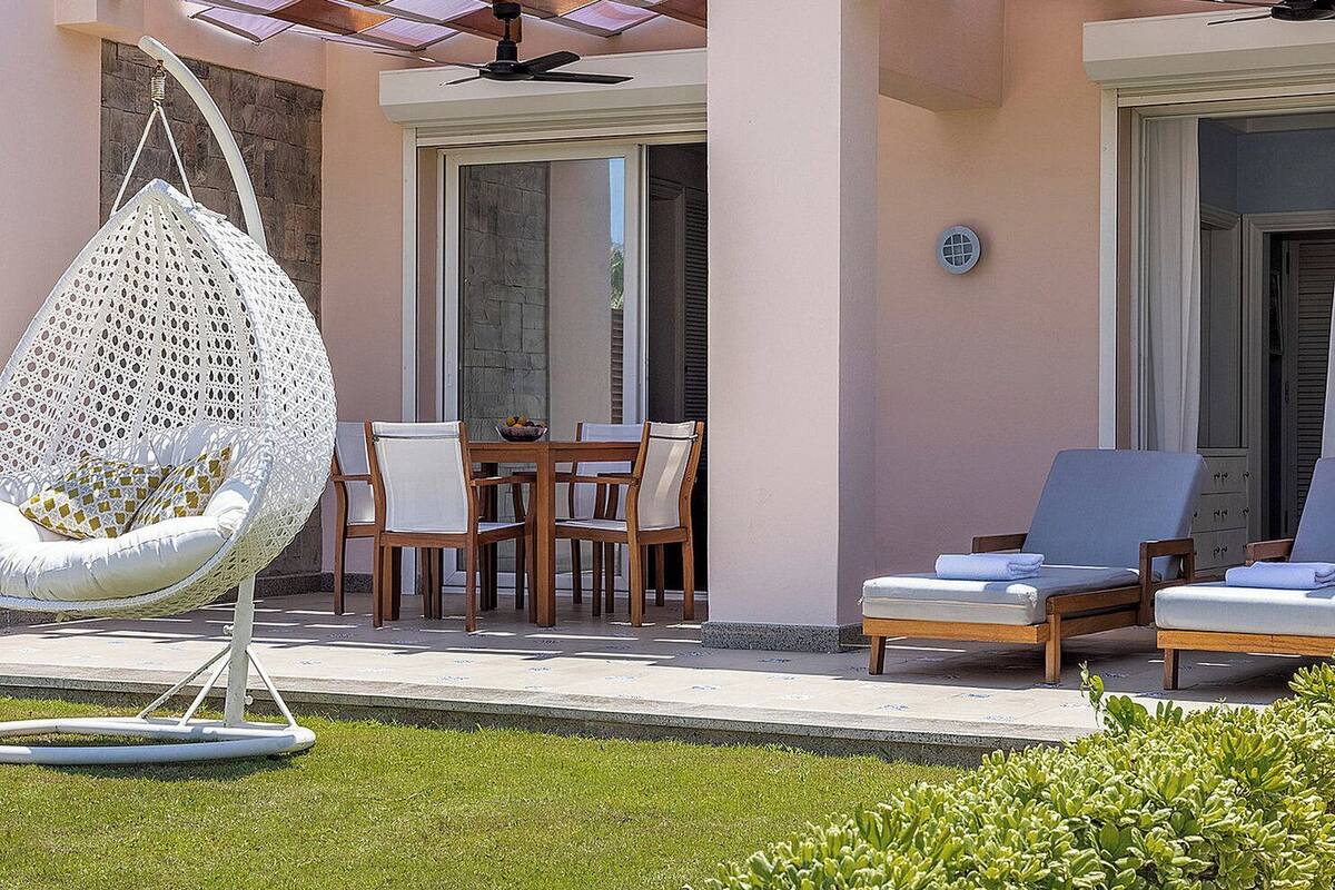 A patio area with a hanging chair, a table with chairs, and two lounge chairs.