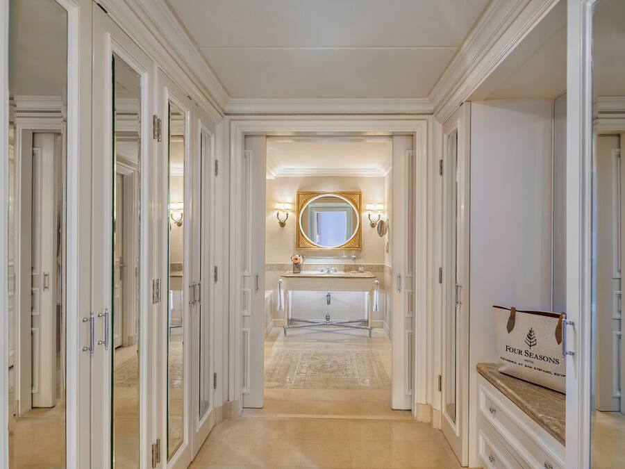 Een gang die leidt naar een badkamer met een wastafel, een grote spiegel en een bord met daarop Four Seasons Hotel.