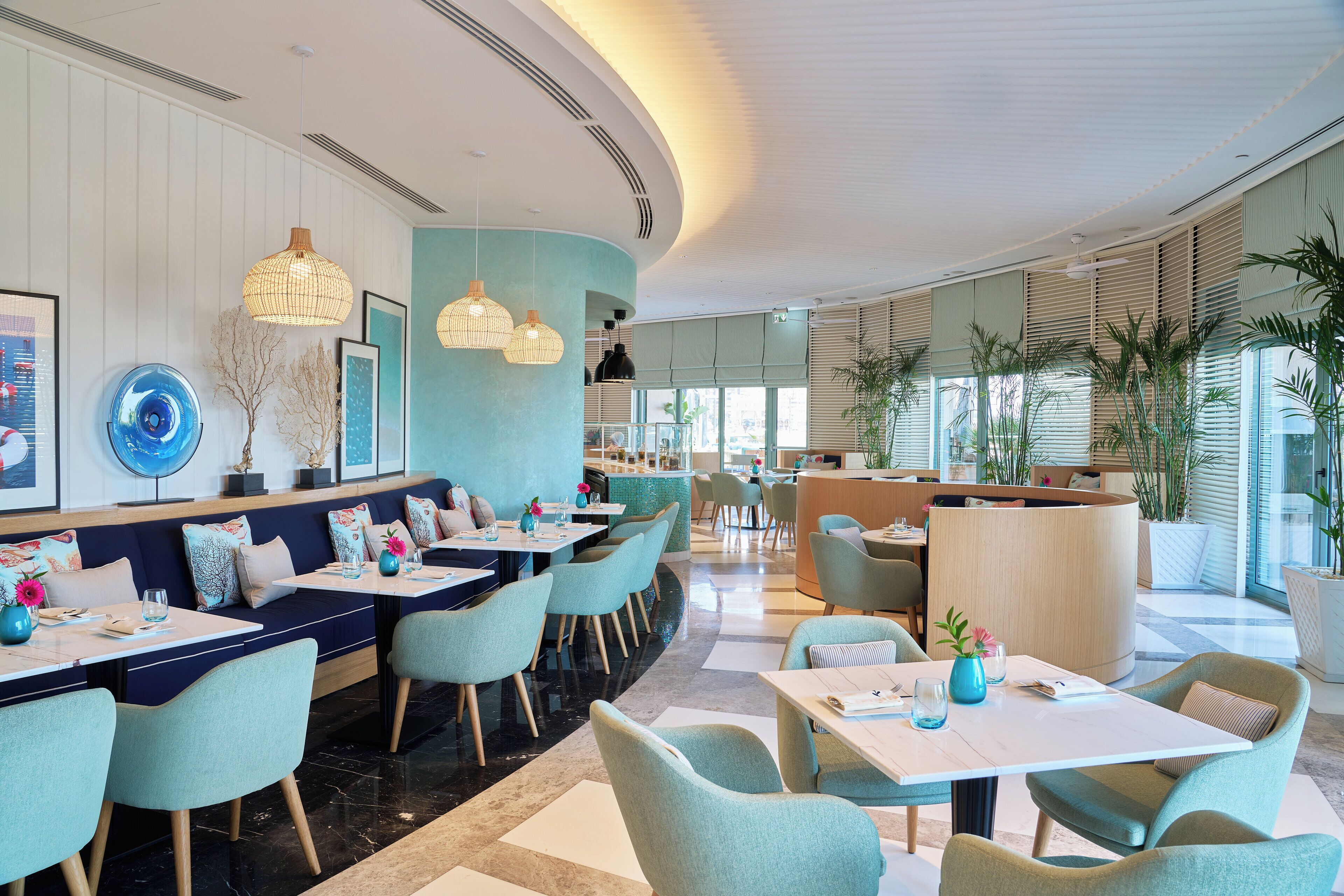 A modern restaurant with a curved seating area, a reception desk, and large windows allowing natural light.