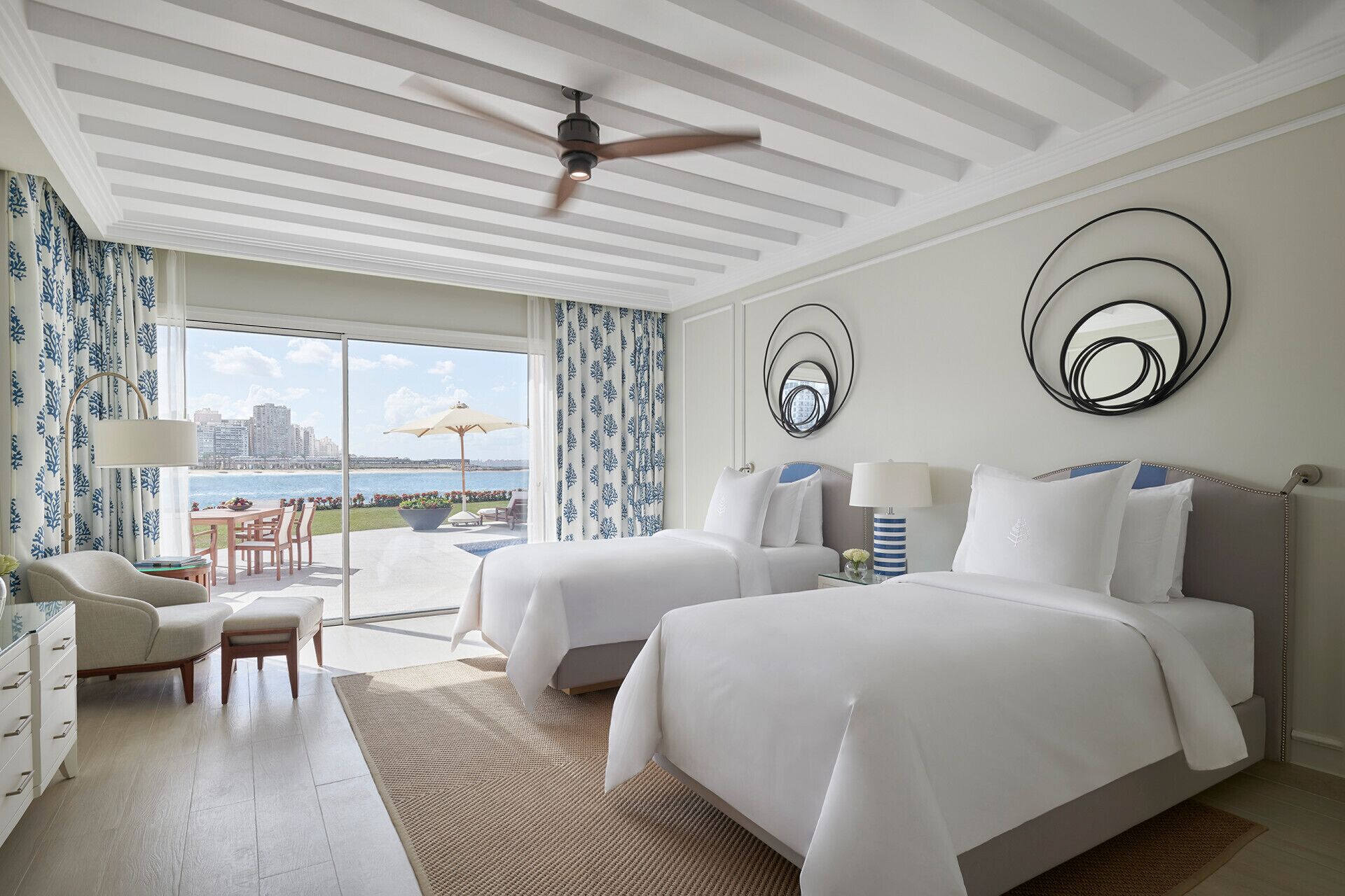 Habitación de hotel con dos camas, vista a la ciudad, zona de comedor y balcón con vistas.