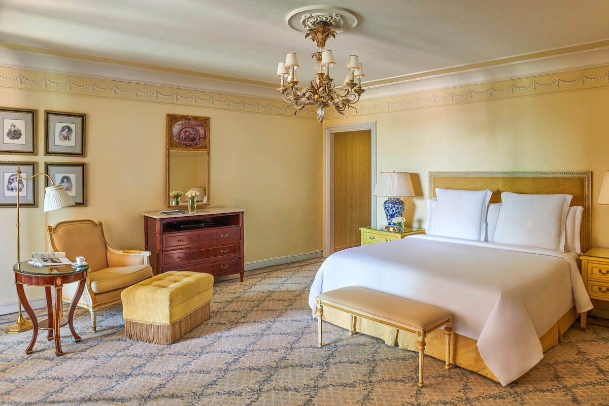 A hotel room with a large bed, a wooden dresser, a chair, a small table, and a mirror.