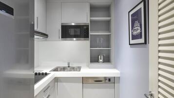 A compact kitchen with a stainless steel refrigerator, microwave, and dishwasher. There are cabinets and a sink. A framed picture hangs on the wall.