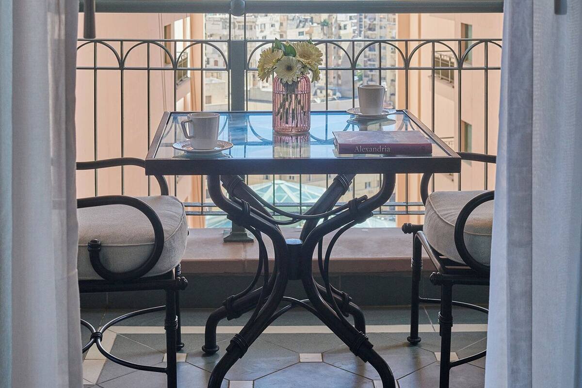 A balcony with a table, two chairs, and a vase with flowers.
