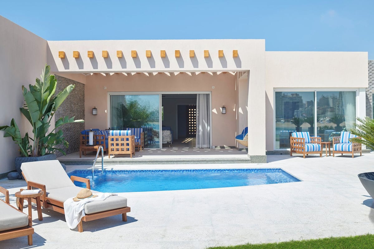 A modern outdoor pool area with lounge chairs, a covered seating area, and a glass-enclosed room.