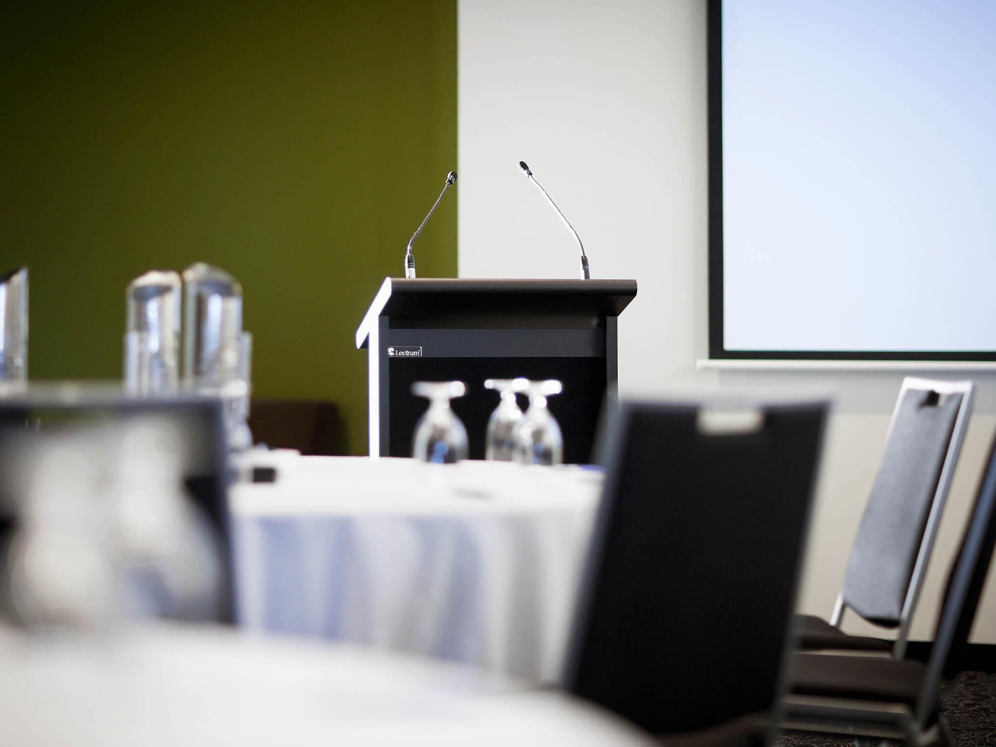 A conference room with a podium, chairs, and a projector screen.