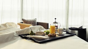 Een netjes opgemaakte ontbijttafel in een bed, met een koffiezetapparaat, een glas sinaasappelsap, een kom cornflakes, een peer en een gebakje.