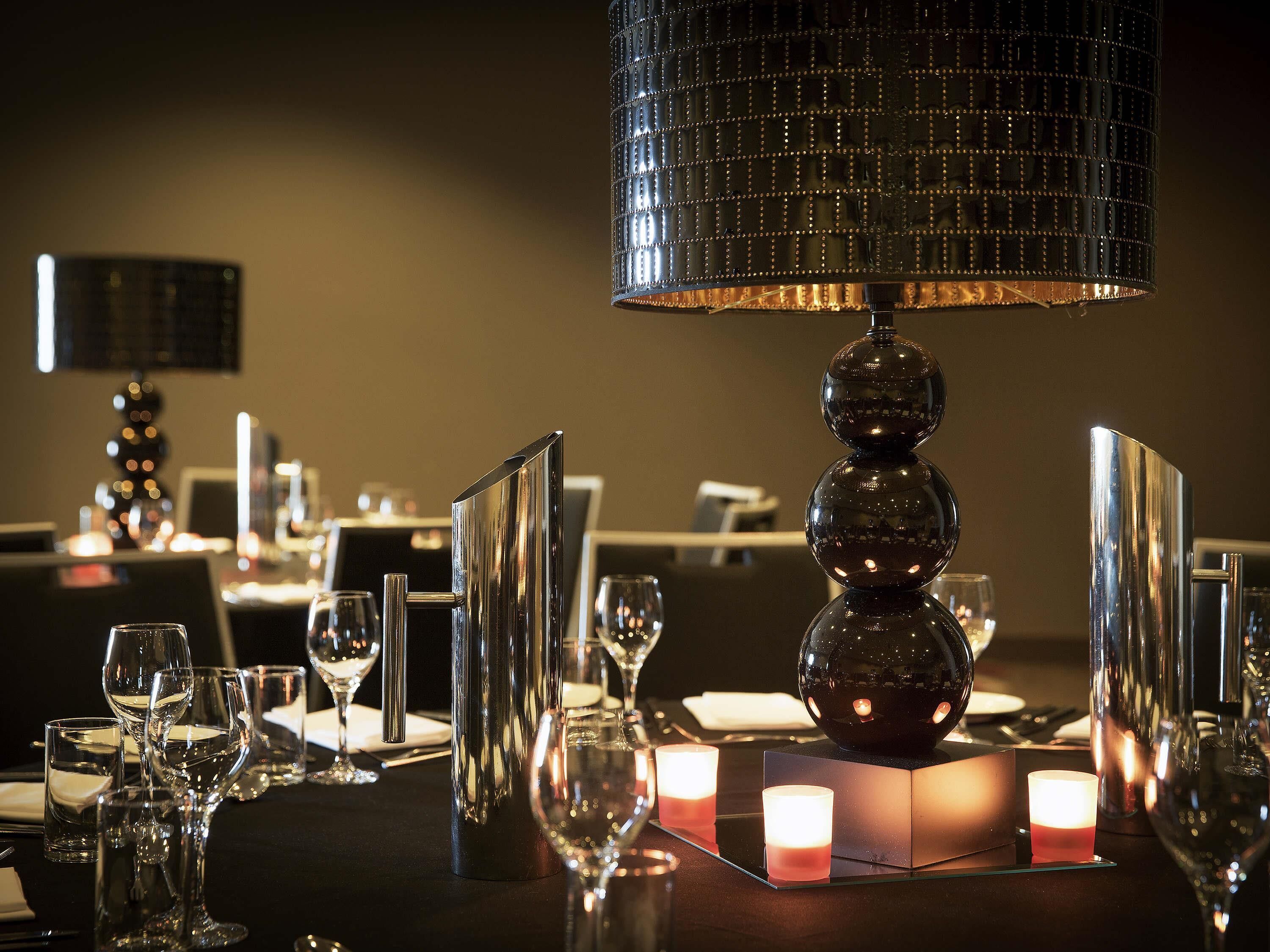 A well-set dining table with candles, glasses, and a decorative lamp.