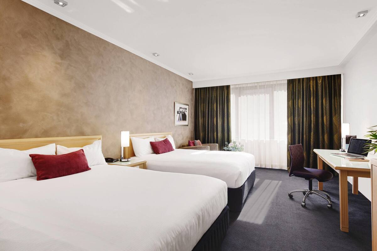 A hotel room with two beds, a desk, a chair, and a window with curtains.