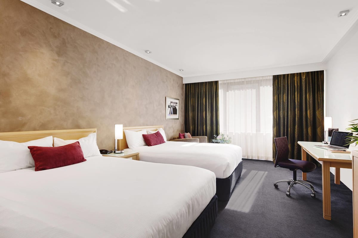 Habitación de hotel con dos camas, un escritorio, una silla y una ventana con cortinas.