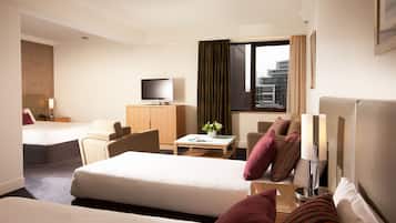 A hotel room with two beds, a television, a desk, and a view of the city.