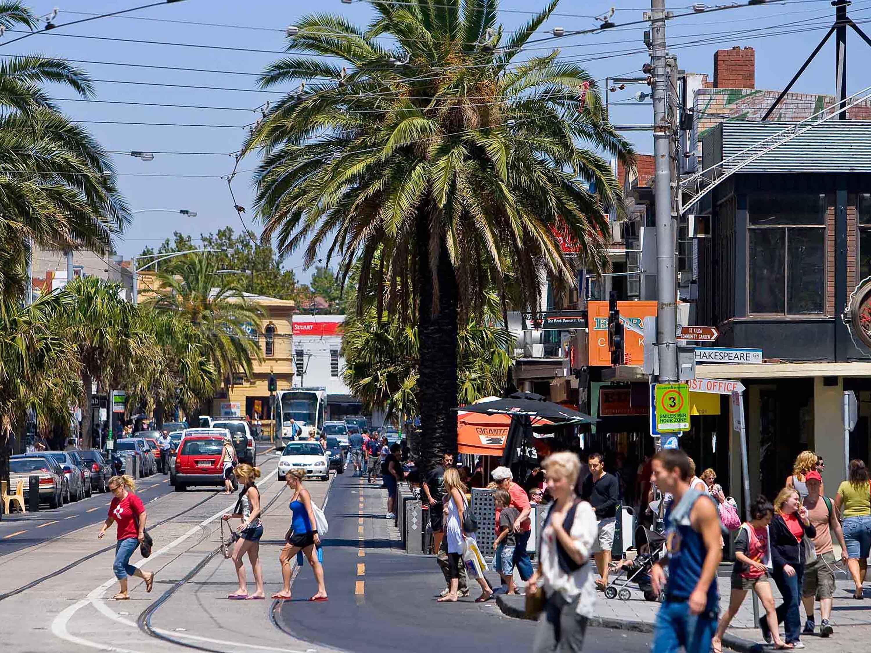 Una calle concurrida con peatones, palmeras y edificios comerciales.